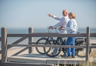 Coppia con biciclette che gode della vista sul mare da una terrazza in legno in un alloggio glamping.