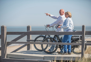 Couple avec vélos profitant de la vue sur la plage depuis une terrasse en bois dans un glamping en bord de mer.