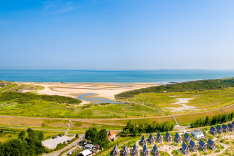 Vista aérea de un alojamiento glamping junto al mar, con playa de arena y aguas azules de fondo.