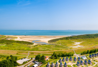 Vista aérea de un alojamiento glamping junto al mar, con playa de arena y aguas azules de fondo.