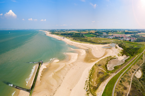 Panoramisk udsigt over kysten og stranden ved et glampingsted med grønne marker i baggrunden.