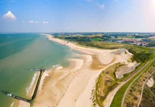 Vista panorámica de una playa arenosa y alojamiento glamping con campos verdes y dunas al fondo.