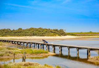 Persona sentada en un largo muelle de madera sobre agua poco profunda junto a un sitio de glamping.