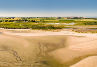 Playa de arena y campos verdes en un alojamiento glamping, cielo despejado y ambiente veraniego relajado.