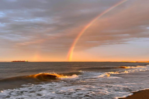 Vista sull’oceano da un alloggio glamping con un arcobaleno vivace, onde e tramonto sulla riva.