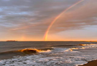 Vista del mar desde un alojamiento glamping con un hermoso arcoíris y olas rompiendo al atardecer.