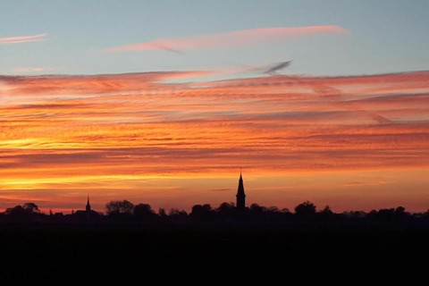Solnedgang over en glamping-plads med silhuet af kirketårn og farverige skyer i horisonten.