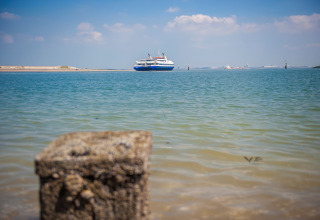 Vista desde un alojamiento glamping al mar con un ferry en la distancia bajo un cielo azul claro.