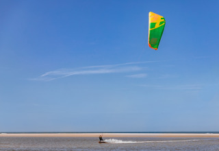 Persona practicando kitesurf en la playa bajo un cielo azul, vista desde un alojamiento de glamping costero.