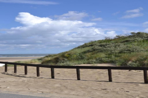 Strandudsigt fra glamping-indkvartering med sand, grønne klitter og himmel under en solrig dag.