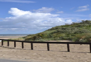 Strandudsigt fra glamping-indkvartering med sand, grønne klitter og himmel under en solrig dag.