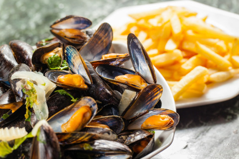 En tallerken med friske dampede muslinger og sprøde pommes frites serveret på glamping-ophold.