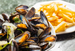 En tallerken med friske dampede muslinger og sprøde pommes frites serveret på glamping-ophold.