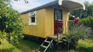 Mobil-home Pipowagen de Weideblick jaune avec terrasse, escalier, et fleurs dans un jardin verdoyant.