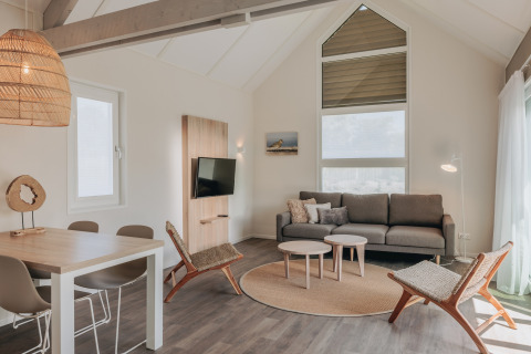 Lys og moderne stue i Beach Resort Nieuwvliet-Bad 16 i Holland med sofa, stole og spisebord.