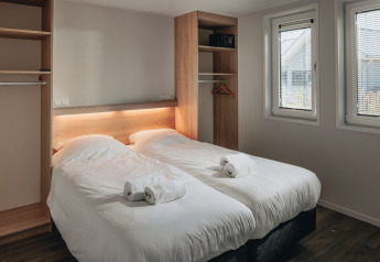 Dormitorio moderno con dos camas individuales, sábanas blancas y toallas en Beach Resort Nieuwvliet-Bad.