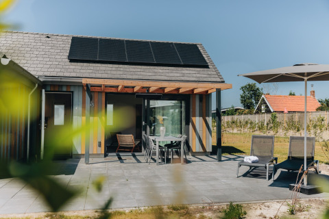 Udendørs terrasse ved Beach Resort Nieuwvliet-Bad 16 i Holland med solpaneler, havemøbler og parasol.