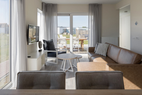 Lyst opholdsområde i Beach Resort Nieuwvliet-Bad 14, med moderne sofa, tv og udsigt til terrasse.