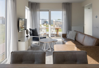 Lyst opholdsområde i Beach Resort Nieuwvliet-Bad 14, med moderne sofa, tv og udsigt til terrasse.