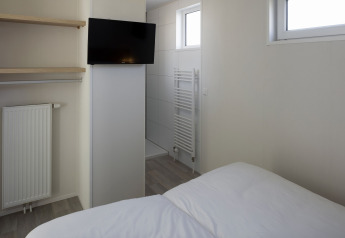 Habitación moderna con TV, estantes, cama y baño en Beach Resort Nieuwvliet-Bad 14, Países Bajos.