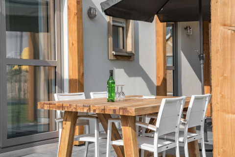 Udendørs spisebord med fire hvide stole, en grøn flaske og glas på Beach Resort Nieuwvliet-Bad 14 i Holland.