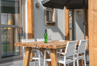 Udendørs spisebord med fire hvide stole, en grøn flaske og glas på Beach Resort Nieuwvliet-Bad 14 i Holland.