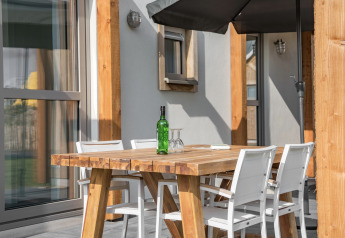 Mesa de madera al aire libre con sillas blancas, botella verde y copas en Beach Resort Nieuwvliet-Bad 14, Países Bajos.