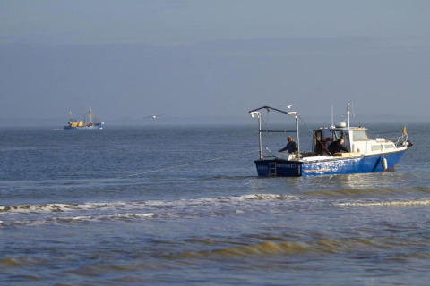 Barca da pesca vicino alla riva con due persone a bordo, un'altra barca visibile in lontananza.