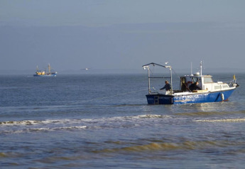 Barco de pesca cerca de la orilla con dos personas a bordo, otro barco visible al fondo en el mar.