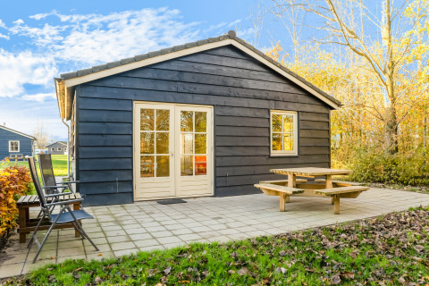 Vista frontal de Holiday Home «5 Aarde Green Camping Lage Zwaluwe» en los Países Bajos, con terraza y banco.