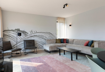 Modern living room at Resort Nieuwvliet-Bad 13 in the Netherlands with sectional sofa and abstract mural.