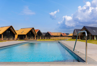 Piscina all'aperto davanti ai lodge moderni del Resort Nieuwvliet-Bad 13 nei Paesi Bassi sotto cielo sereno.