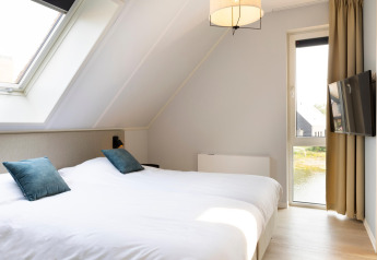 Modern bedroom at Resort Nieuwvliet-Bad 13 with skylight, large bed, TV and scenic window view.
