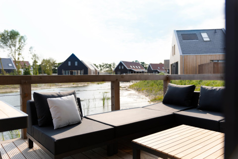 Area lounge esterna moderna con cuscini neri e vista sull’acqua al Resort Nieuwvliet-Bad, Paesi Bassi.