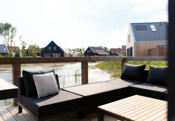 Modern outdoor lounge area with black cushions, wooden table, and water view at Resort Nieuwvliet-Bad, Netherlands.