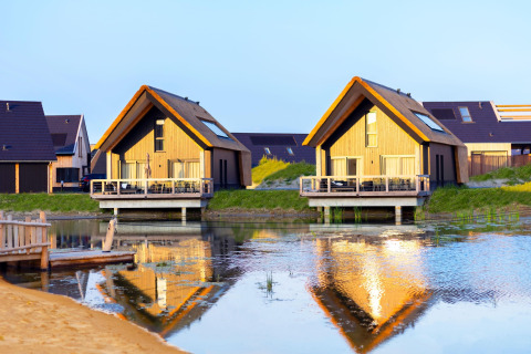 Due lodge in legno sul lago, riflessi nell'acqua, al Resort Nieuwvliet-Bad 13 nei Paesi Bassi.
