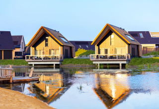 Due lodge in legno sul lago, riflessi nell'acqua, al Resort Nieuwvliet-Bad 13 nei Paesi Bassi.