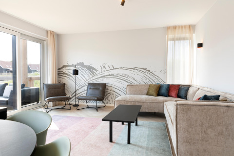 Soggiorno luminoso con divano angolare moderno, cuscini colorati e murale artistico presso il lodge olandese.