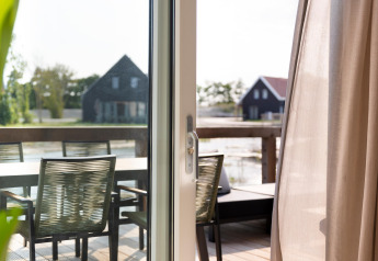 View from a lodge with glass door to terrace and chairs at Resort Nieuwvliet-Bad 13, Netherlands.