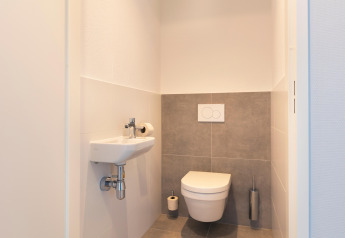 Modern, minimalist restroom with wall-mounted toilet and small sink at Resort Nieuwvliet-Bad 13 in the Netherlands.