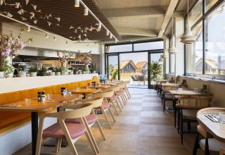Area pranzo luminosa al Resort Nieuwvliet-Bad 13 nei Paesi Bassi con tavoli in legno e grandi finestre.