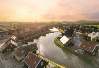 Aerial view of Resort Nieuwvliet-Bad 13 in the Netherlands, showing lodges along canals at sunset.