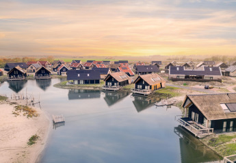Aerial view of vacation lodges at Resort Nieuwvliet-Bad 13 in the Netherlands, nestled by tranquil waters at sunset.