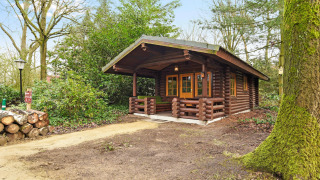 Et smukt træchalet ved Park Duc de Brabant 3 med veranda omgivet af grønne træer og buske.