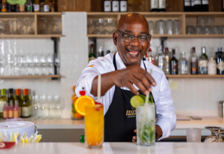 Barista al Resort Nieuwvliet-Bad 13 nei Paesi Bassi, sorridente mentre prepara cocktail dietro il bancone.