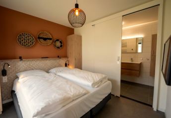 Moderne lodge-soveværelse med dobbeltseng, varme farver og kig til badeværelse i Holiday Park Zeebad.