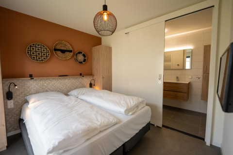 Modern lodge bedroom with double bed, warm decor, and en suite bathroom at Holiday Park Zeebad, Netherlands.