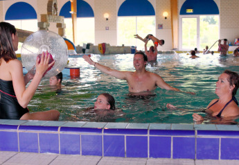 Families enjoy playing together in an indoor swimming pool at a lodge, with kids and adults in the water.
