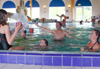 Familier leger i en indendørs swimmingpool på en lodge, med børn og voksne der nyder vandet sammen.