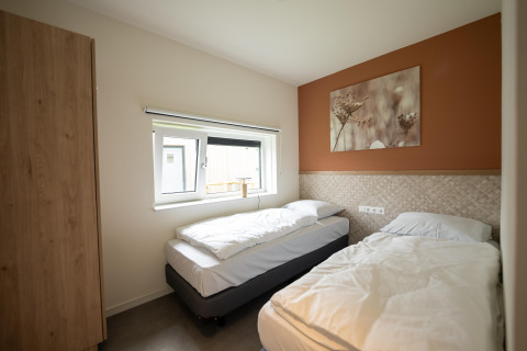 Chambre lumineuse avec deux lits simples, fenêtre et tableau nature au Holiday Park Zeebad 14, Pays-Bas.